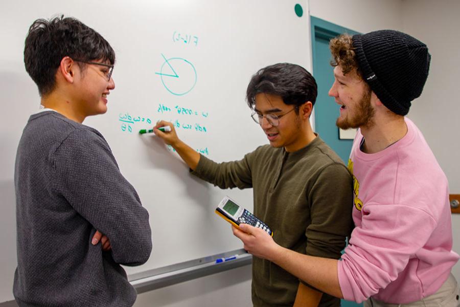 三个太阳集团娱乐场登陆网站的学生正在白板上做一道数学题
